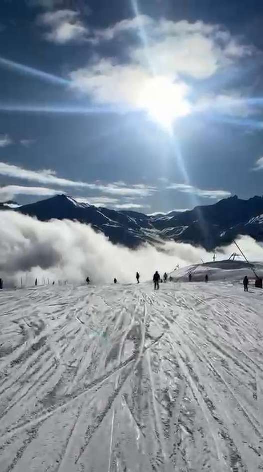 Wide view down Anémone towards Tignes Le Lac, with skiers, mountain peaks and low cloud. Still from Fergus Halpin’s video.