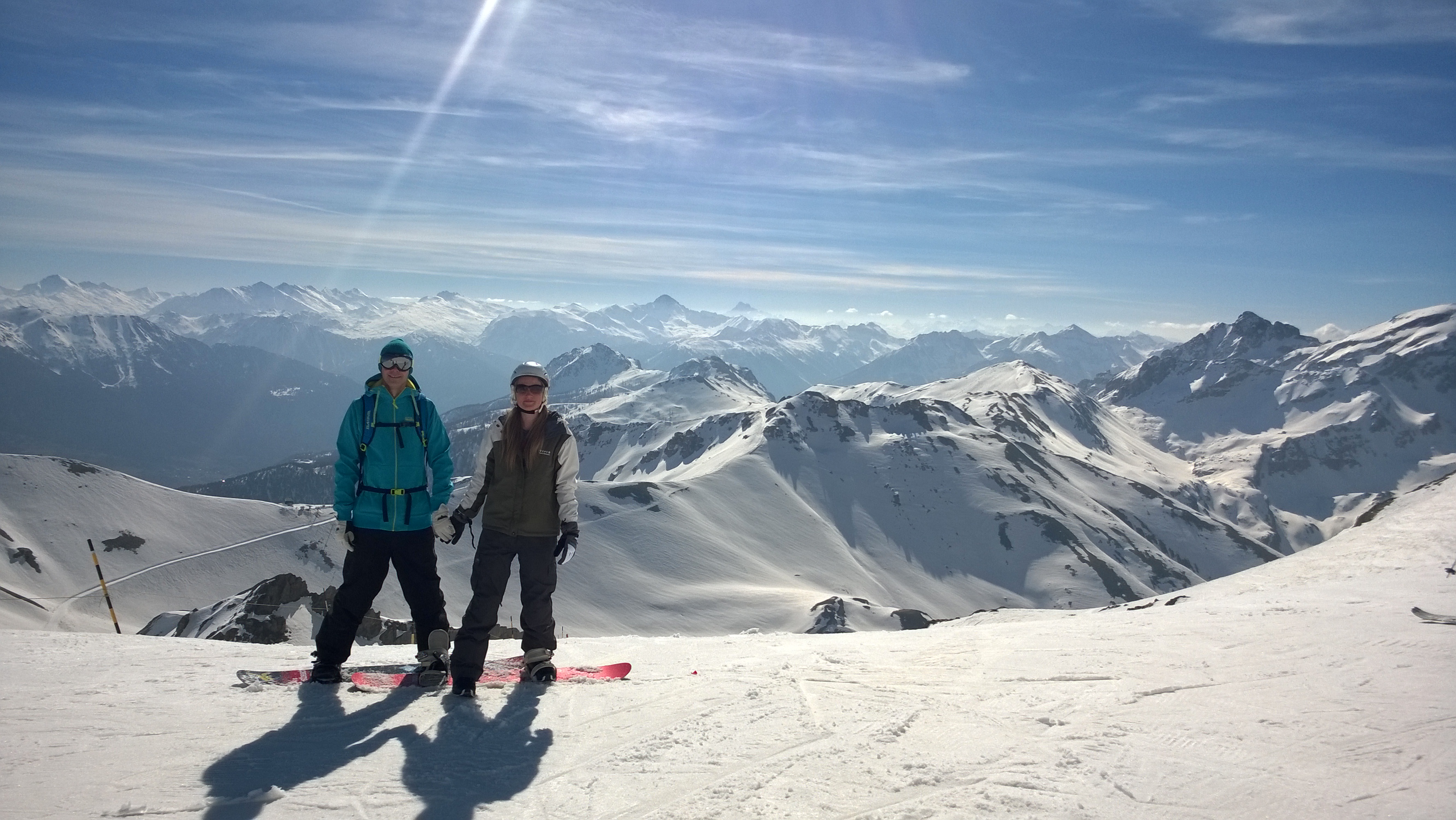 Snowboarders standing on top of a sunny mountain