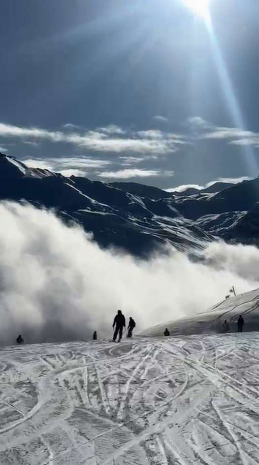 Skiers descending the Anémone blue piste above a bank of cloud, with sunlit mountains beyond. Still from Fergus Halpin’s video.